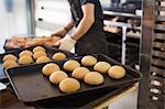 Person working in a bakery, placing freshly baked rolls on large trays.