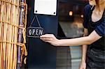 Close up of woman turning open sign on glass door to a bakery.