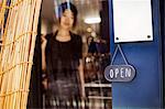 Open sign on glass door to a bakery, a woman standing in the doorway.