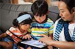 Man, boy and young girl sitting on a grey sofa, looking at digital tablet.