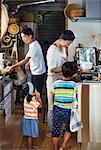 Man, woman wearing apron, boy and young girl standing in a kitchen, preparing food.