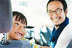 Man wearing glasses and boy sitting in a car, smiling at camera.