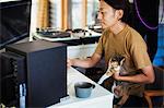 Man sitting at a desk in front of computer, calico cat with white, brown and black fur on his lap.