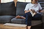 Man sitting on grey sofa, calico cat with white, black and brown fur on his lap.