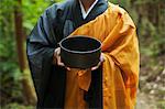 Close up of Buddhist monk wearing black and yellow robe, holding singing bowl.
