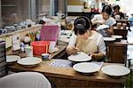 Women sitting in a workshop, working on Japanese porcelain bowls.