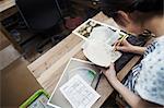 High angle close up of woman working in a Japanese porcelain workshop, transferring design onto plate.