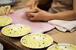 Close up of person working in a Japanese porcelain workshop, applying yellow glaze to white plates.