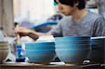 Close up of man working in a Japanese porcelain workshop, painting white bowls with blue glaze.