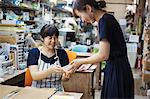 Two smiling women sitting and standing in a workshop, looking at Japanese porcelain bowl.