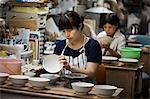 Two women sitting in a workshop, working on Japanese porcelain bowls.
