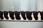 Large group of mannequin heads with brown wigs in a row on a table.