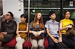 Five people sitting sidy by side on a subway train, Tokyo commuters.