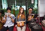 Three people sitting sidy by side on a subway train, reading,Tokyo commuters.