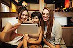 Three women sitting side by side in a restaurant, taking selfie with smartphone.