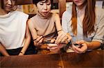 Three women sitting side by side at a table in a restaurant, holding chopsticks.