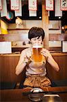 Woman sitting at a table in a restaurant, drinking from large glass of beer.