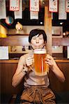 Woman sitting at a table in a restaurant, holding large glass of beer.