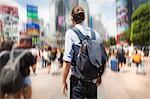 A young man with a backpack on a crowded street in downtown Tokyo.