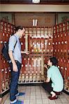 A young Western man with a backpack and a Japanese man discussing the rules of the public bath house, and putting outdoors shoes in the lockers.