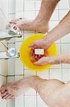 A man standing in a shower with soap in his hands, washing.