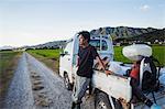 A rice farmer standing by his truck looking across the flat landscape, rice paddies and a village in the distance.