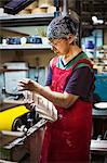 Woman working in a Japanese porcelain workshop, wearing apron, holding white porcelain object.