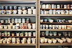 Large selection of ceramic cups and mugs on shelves in a Japanese porcelain workshop.