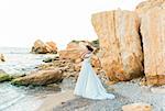 Beautiful brunette bride in light chiffon wedding dress embroidered with beads posing near the sea. Romantic beautiful bride in luxury dress posing on the beach.