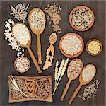 High fiber health food of whole wheat pasta, cereal and grains in bowls and spoons on rustic oak background.