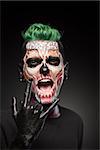 Man with halloween makeup showing tongue. Stylish zombie makeup on mans face, isolated in black background.