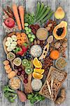 Health food concept for a high fiber diet with fruit, vegetables, cereals, nuts, seeds, whole wheat pasta, grains, legumes and spice. Foods high in omega 3, anthocyanins, antioxidants and vitamins on rustic background top view.