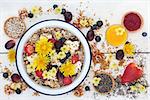 Macrobiotic health food for breakfast concept with granola, edible flowers, acai berry powder, pollen grain, berry fruit, chia seed and nuts with foods high in protein, omega 3, anthocyanins, antioxidants, and vitamins on rustic background, top view.