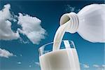 Pouring fresh milk from a bottle into a glass, blue sky with clouds on the background