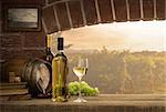 White wine tasting in the wine cellar: wineglass and bottles next to the window and panoramic view of vineyards at sunset