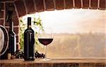 Red wine tasting in the wine cellar: wineglass and bottles next to the window and panoramic view of vineyards at sunset