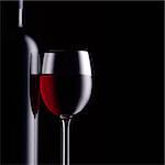 Excellent red wine tasting and celebration: wine bottle and full wineglass on black background