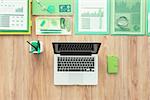 Laptop, green office supplies and financial reports on a wooden desktop, green business and ecology concept