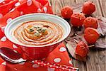 Pumpkin soup with seeds, honey and red physalis on rustic wooden table