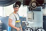 Portrait of a young and handsome auto mechanic looking at camera with confidence while welding during work in a modern automobile repair shop