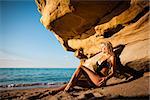 Young woman in black bikini posing on a sand rocks near the sea