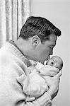 1960s FATHER HOLDING AND KISSING HIS INFANT BABY SON