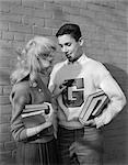 1950s TEENAGE COUPLE HOLDING BOOKS SMILING LEANING AGAINST WALL BOY WEARING VARSITY LETTER SWEATER