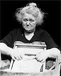 1930s DEPRESSION ERA SENIOR WOMAN SAD FACIAL EXPRESSION WASHING CLOTHES LAUNDRY ON SCRUBBING WASHBOARD LOOKING AT CAMERA