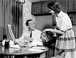 1960s WIFE POURING BREAKFAST COFFEE FOR HUSBAND DRINKING JUICE READING MORNING NEWSPAPER