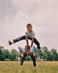 1960s BOYS PLAYING LEAP FROG ONE JUMPING OVER THE OTHER'S BACK LOOKING AT CAMERA