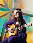 1970s YOUNG WOMAN WEARING PURPLE DRESS AND BEADED HEADBAND PLAYING ACOUSTIC GUITAR PATTERNED BACKGROUND FOLK SONG