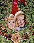 1960s SMILING BLONDE BOY AND GIRL BROTHER AND SISTER PEEKING OUT FROM CENTER OF CHRISTMAS WREATH