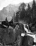 1920s 1930s COUPLE MAN WOMAN ON HORSES BY WATERFALL IN PINE FOREST GIANTS STEPS PARADISE VALLEY ALBERTA CANADA