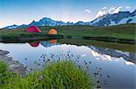 Camping tents in the green meadows surrounded by flowers and alpine lake, Mont De La Saxe, Courmayeur, Aosta Valley, Italy, Europe